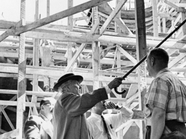 Frank Lloyd Wright standing at construction site of Guggenheim Museum wearing hat and pointing cane at scaffolding