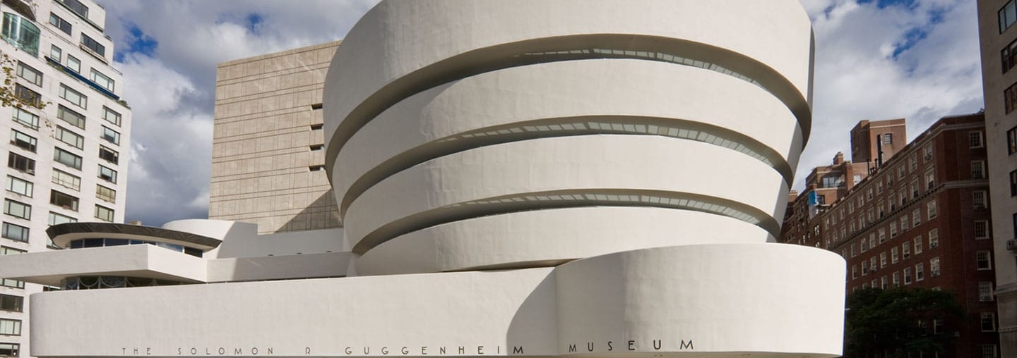 Exterior view of the Solomon R. Guggenheim Museum in New York City, showcasing its distinctive spiral design and modernist architecture with a clear blue sky in the background.