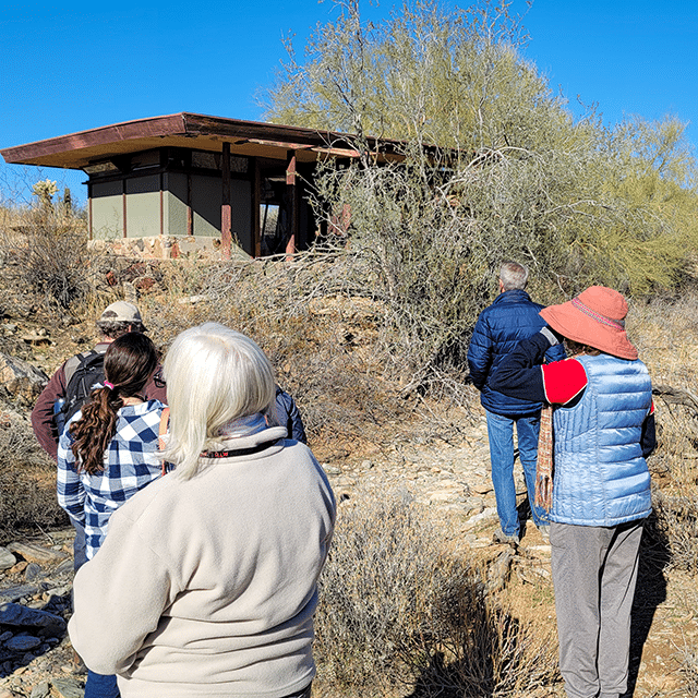 A group of visitors on the Shelters in the Desert Guided Tour approaching a structure to learn about its history.